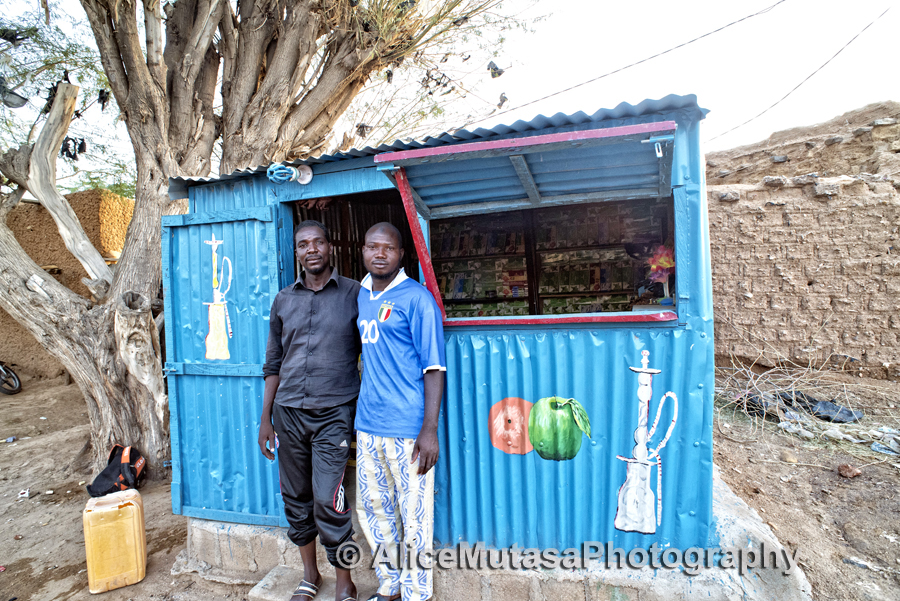 Dankouma Daoude & his friend outside his shop selling herbal tobacco for shisha pipes