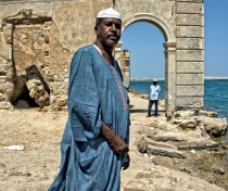 Adil in Suakin, with ruins of the old town built of coral behind him